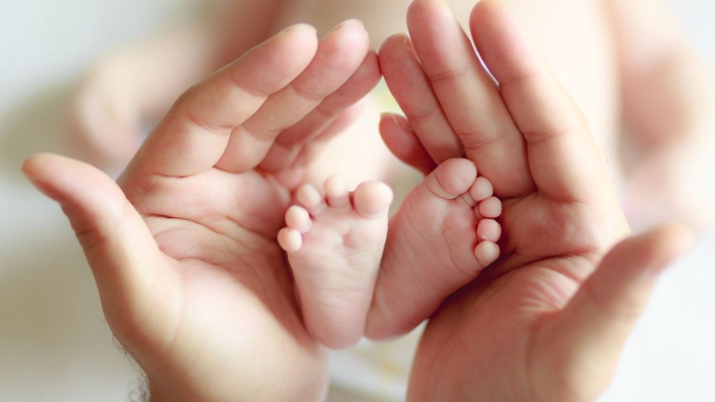 Close-up of adult hands gently cradling the tiny feet of a newborn baby, symbolizing love, protection, and new life.